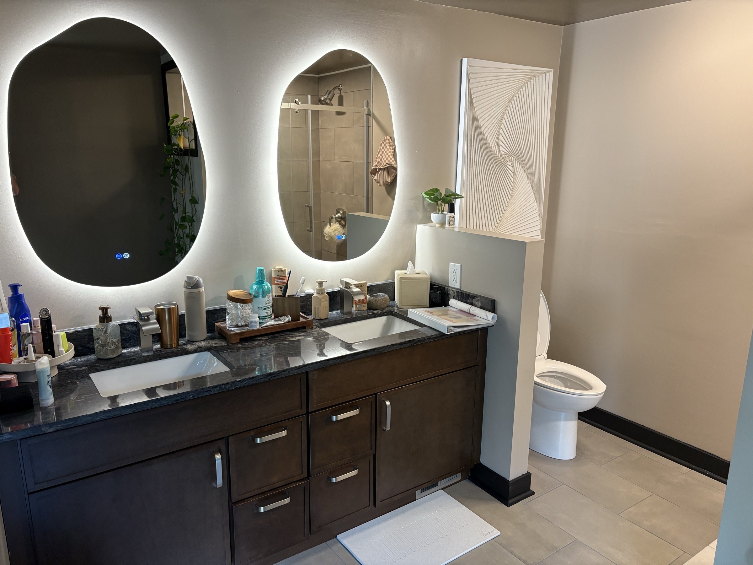 Primary bath with backlit mirrors and dark granite double vanity