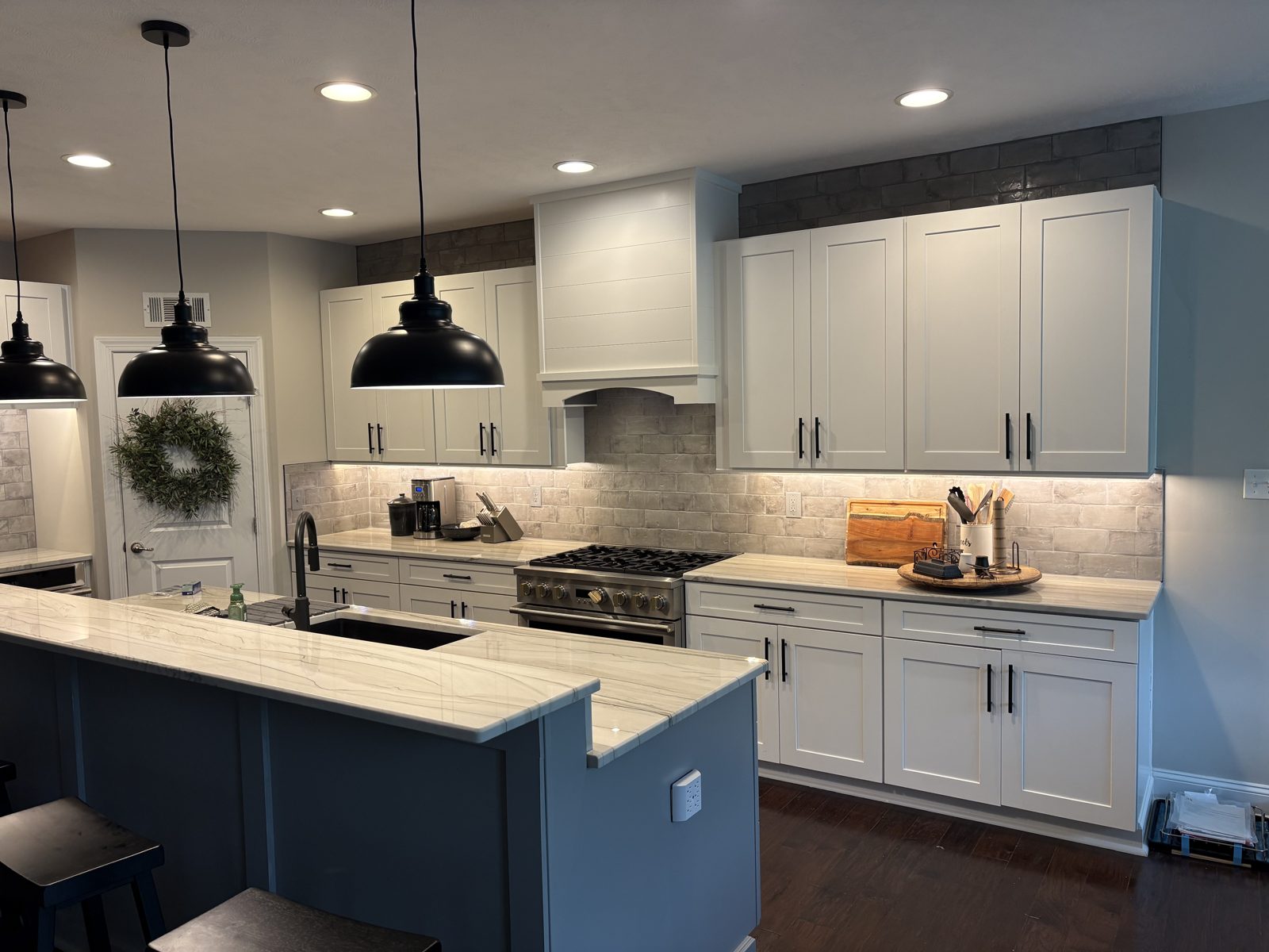 White shaker kitchen with a blue island, pendant lights and gas range