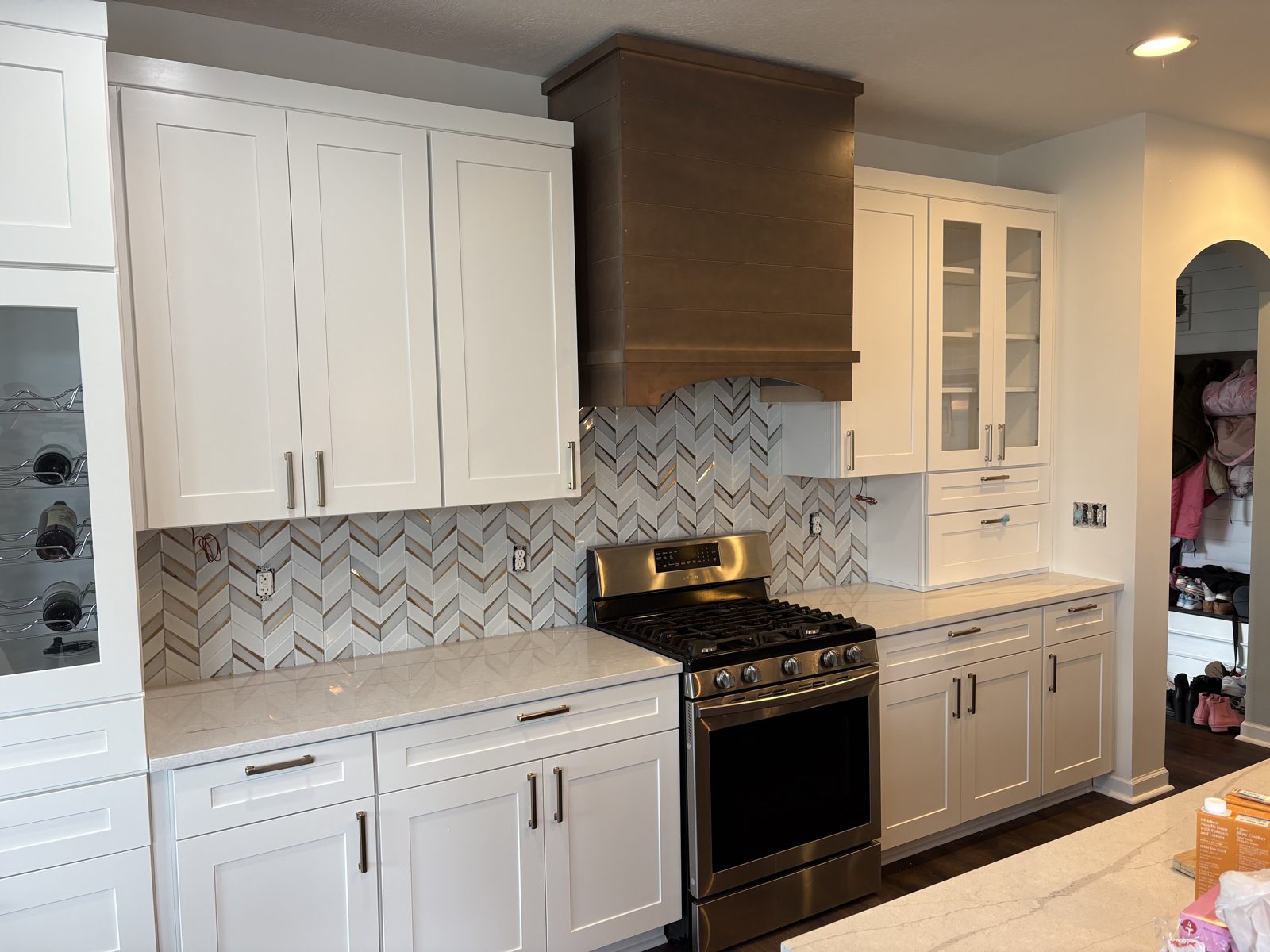 White kitchen with herringbone tile backsplash and a wood range hood