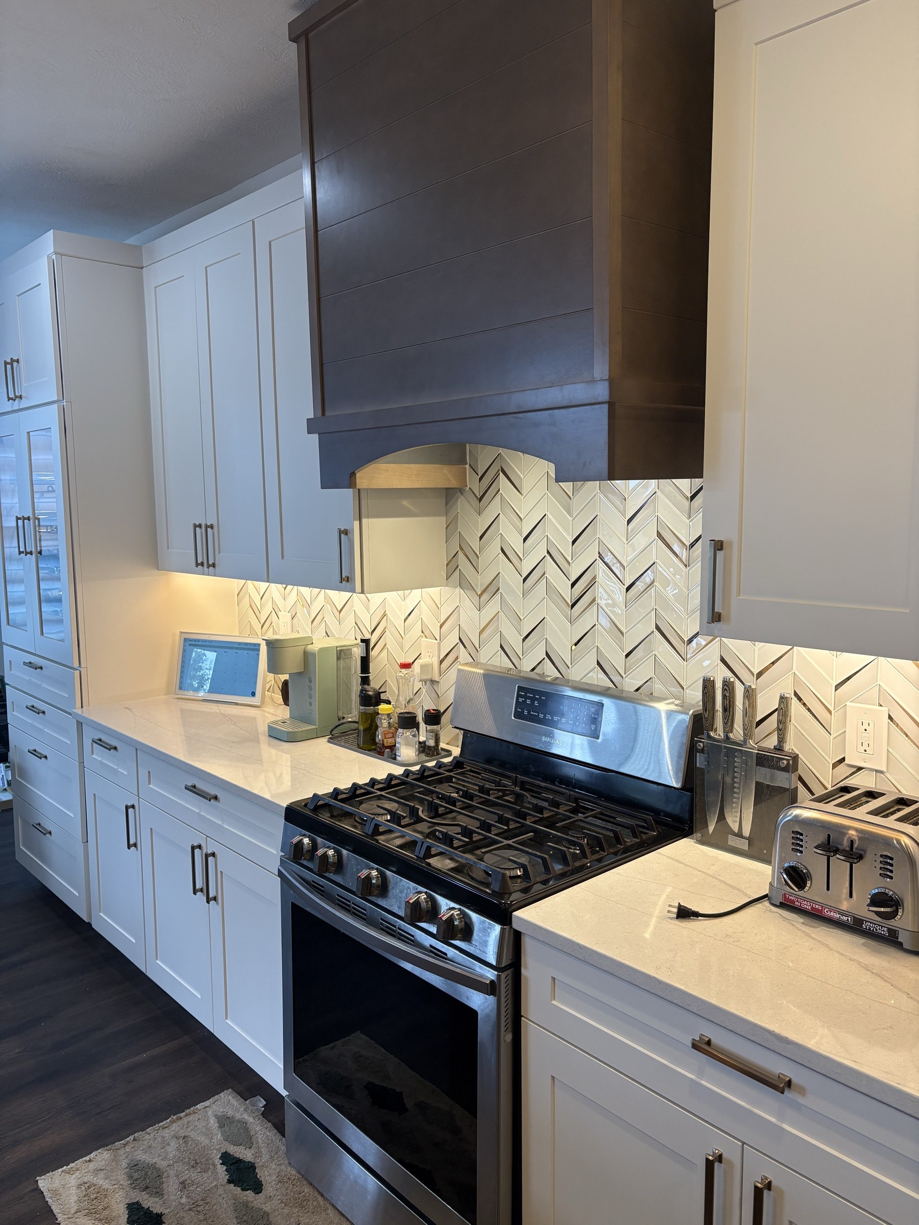 Dark wood range hood with herringbone tile and gas range
