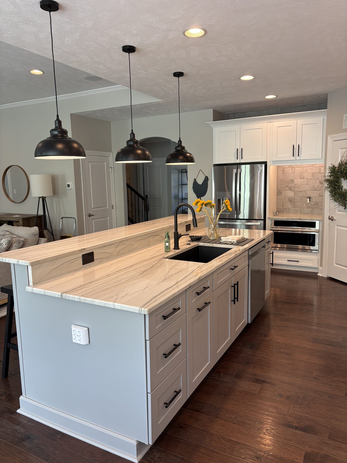 Kitchen island with a stone top, black faucet and three black pendant lights