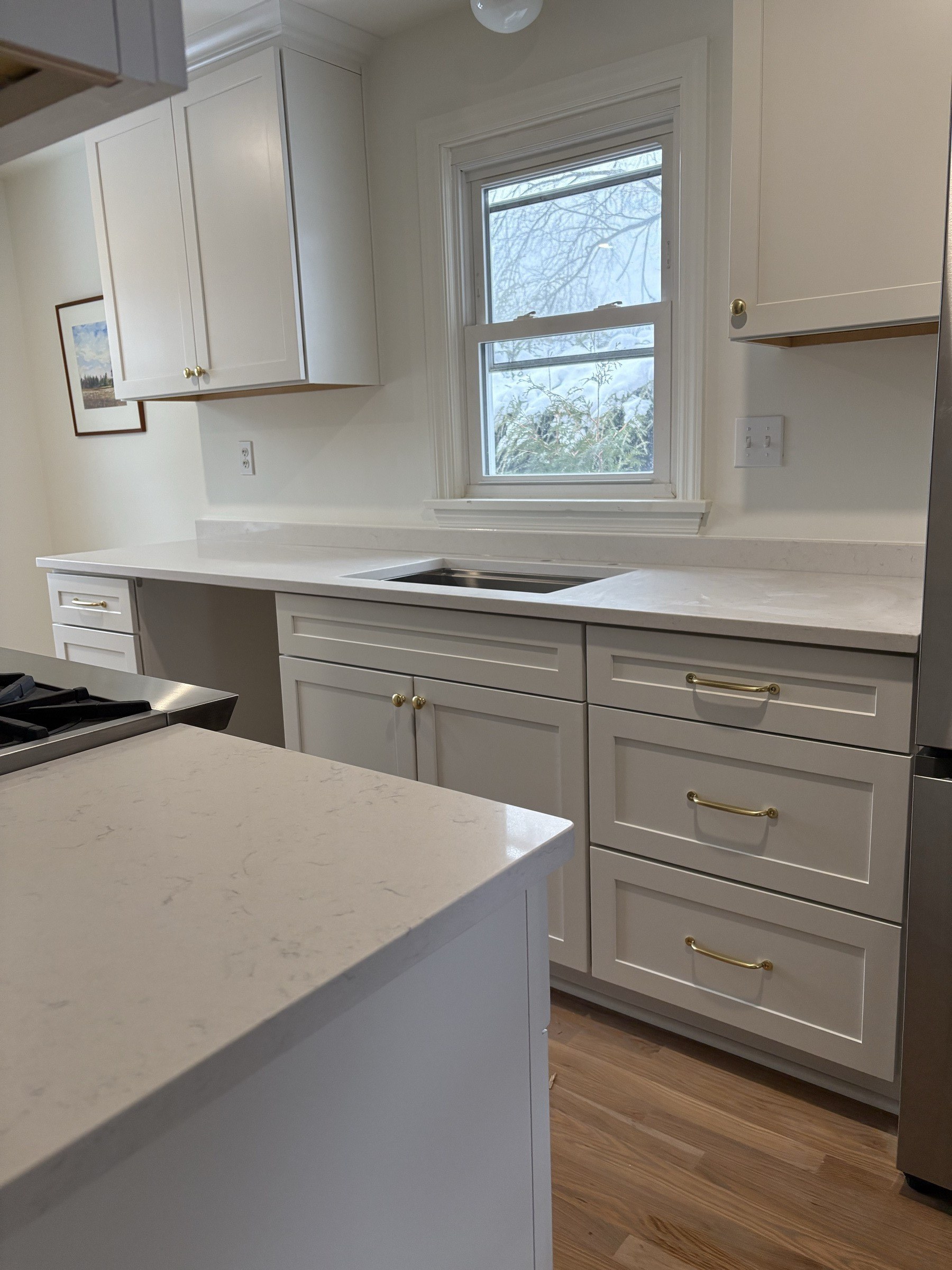 Finished white shaker kitchen with island, brass hardware, and quartz counters