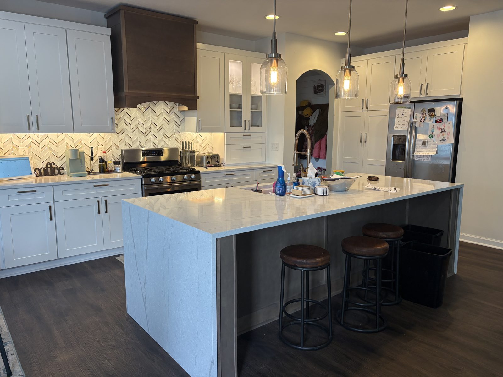 White kitchen with a waterfall quartz island, dark wood range hood and pendant lights