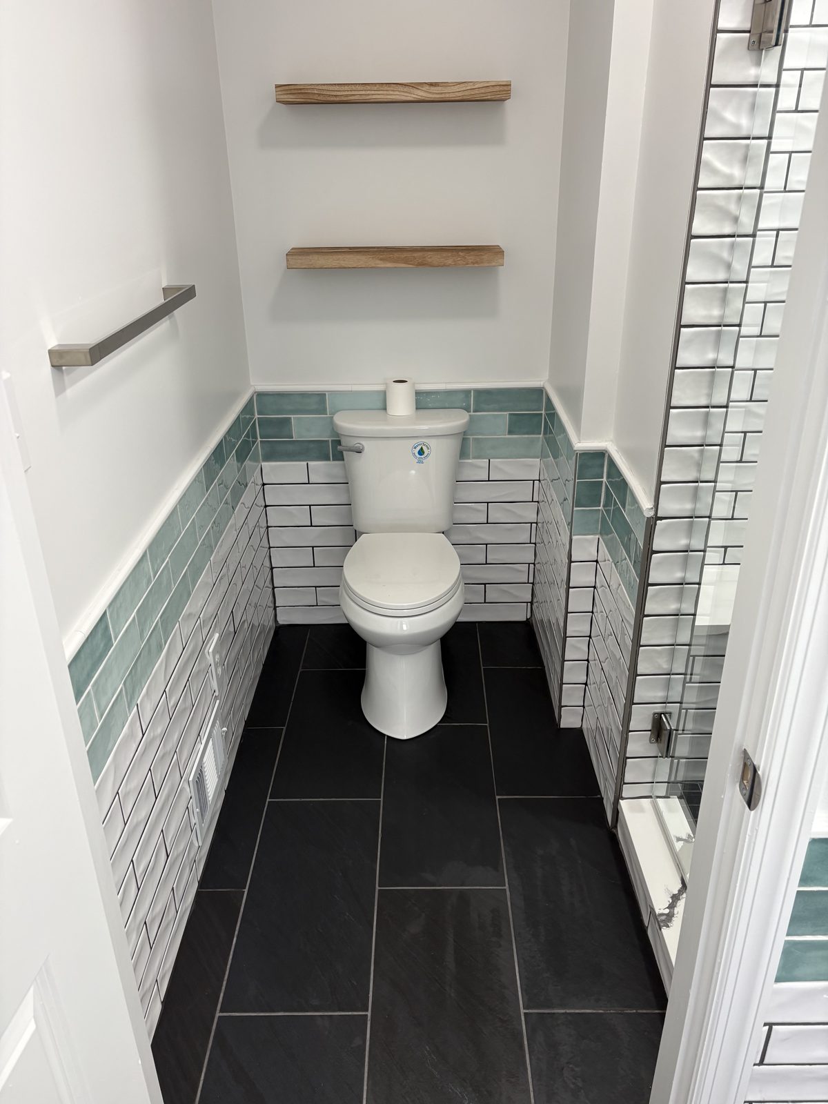 Powder room with a green tile band and floating wood shelves