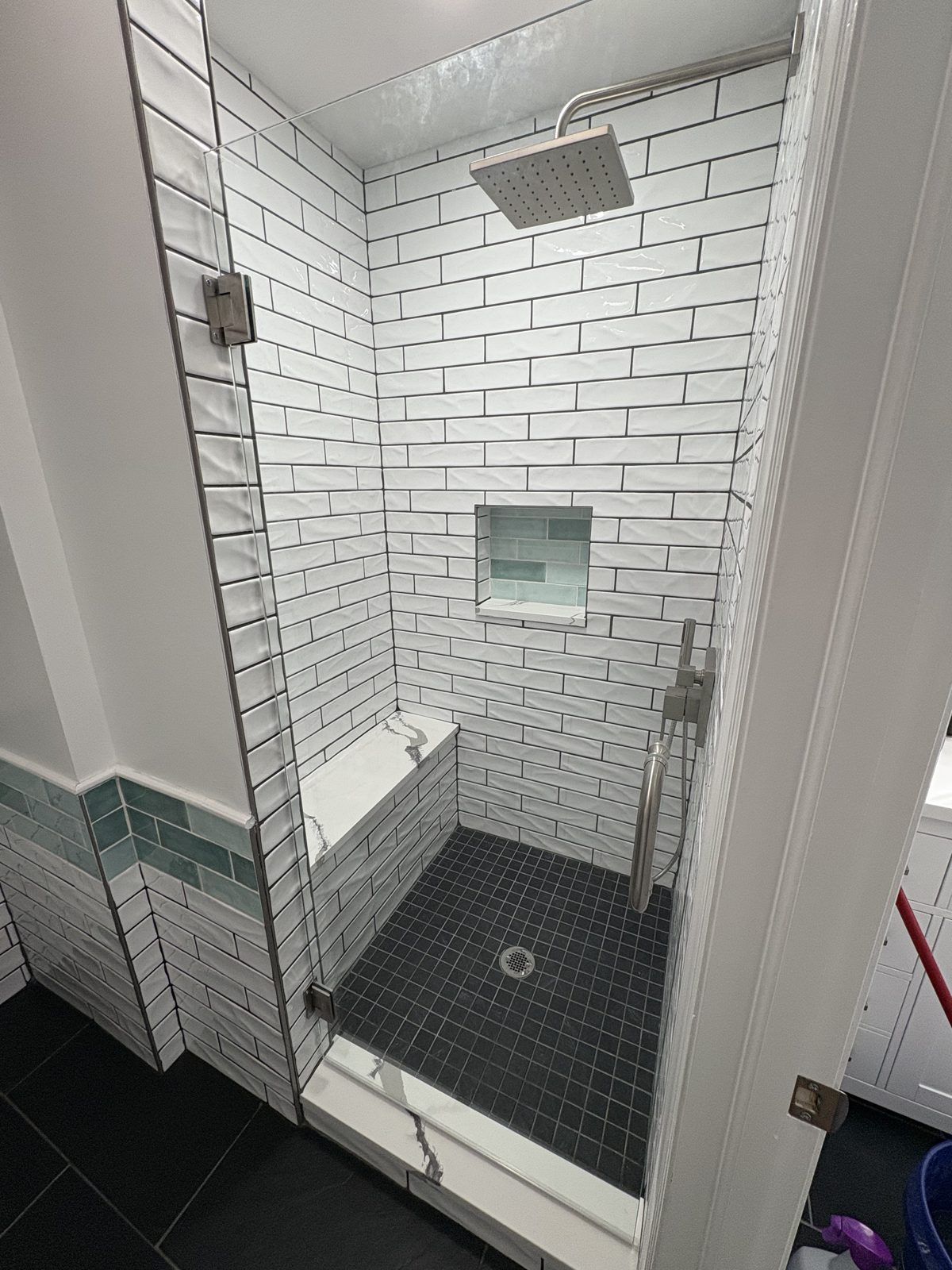 Walk-in shower with white subway tile, black floor tile and a glass door